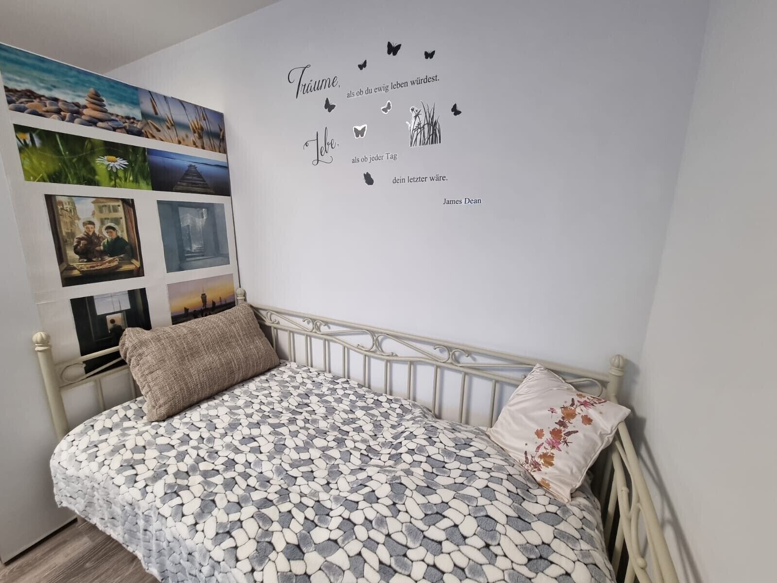 Une chambre à coucher avec un lit, un mur orné de photos et d’une citation, et un coussin décoratif.