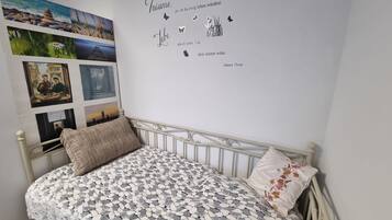 Une chambre à coucher avec un lit, un mur orné de photos et d’une citation, et un coussin décoratif.