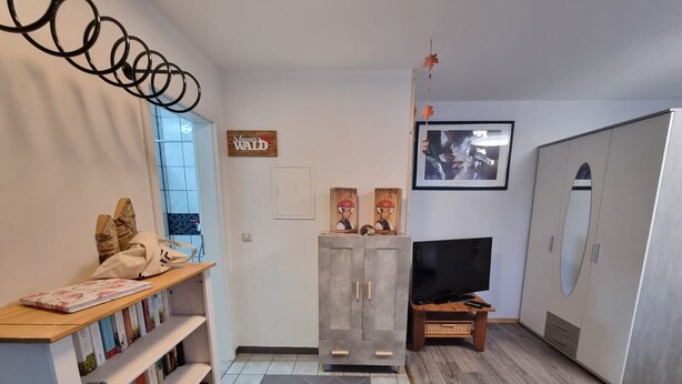 A modern living room with a bookshelf, a TV, a wardrobe, and a decorative sign. - Studio Apartment "Kuckuck" with Wi-Fi (Ohlsbach)