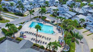 Vista aérea de un área residencial con piscina rodeada de sillones de descanso y palmeras.