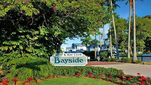 Señal del club Gulf & Bay Club Bayside, con vista a los edificios del resort y palmeras.