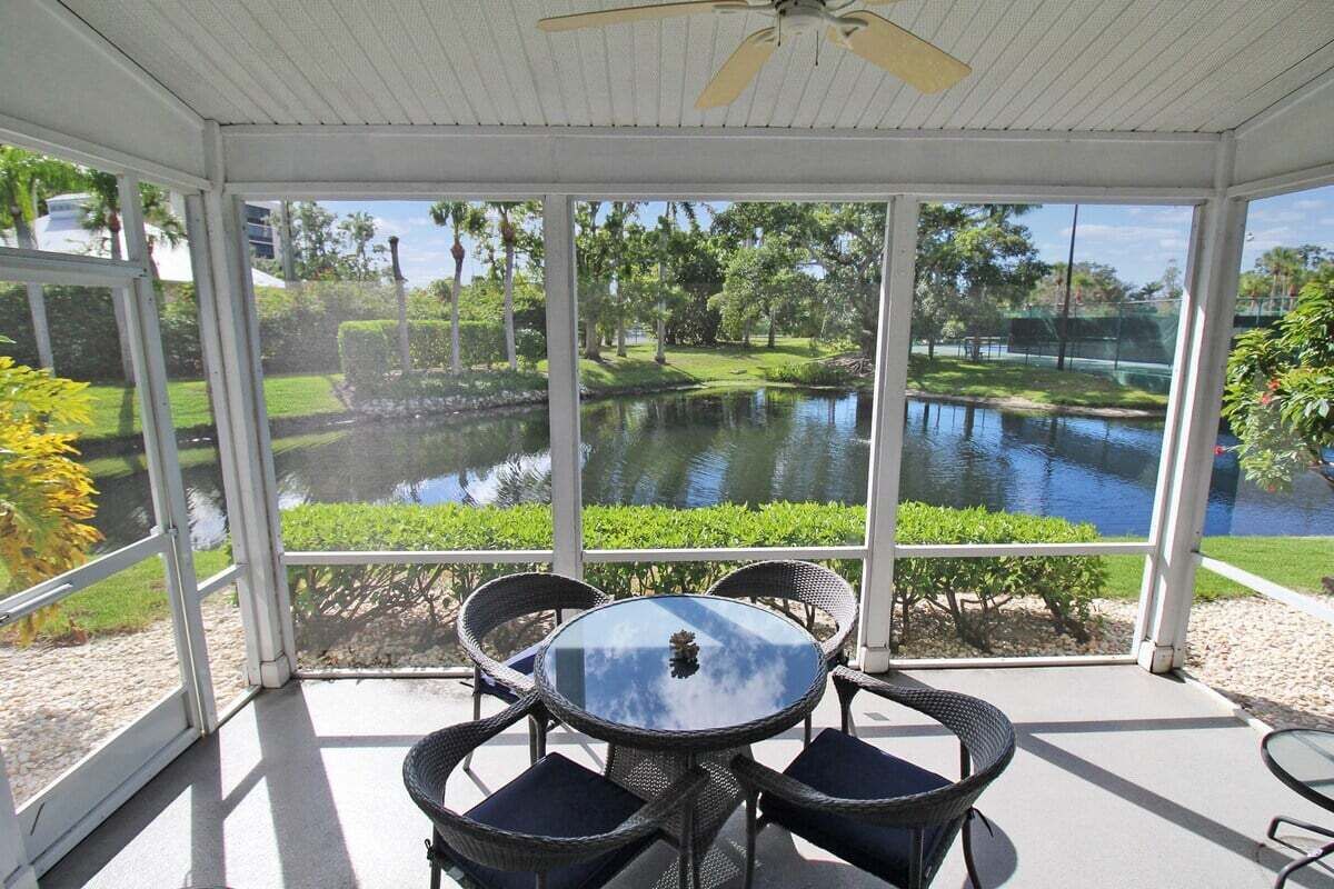 A covered patio with a table and chairs, overlooking a pond and greenery.