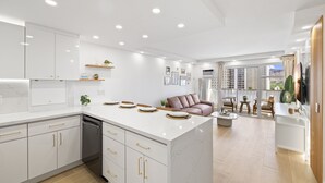 A modern kitchen with white cabinetry, a central island, and a dining area with a sofa and chairs. - High Floor 2BR/2BA+Den 4beds Partial Ocean View + 1 Parking 2 min from the Beach (Honolulu)
