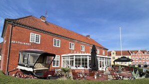 Un restaurante con fachada clásica de ladrillo rojo, mesas y sillas para disfrutar al aire libre, y un carruaje antiguo estacionado frente a él.
