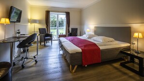 Habitación de hotel con cama, escritorio, silla, televisor y vista al exterior.