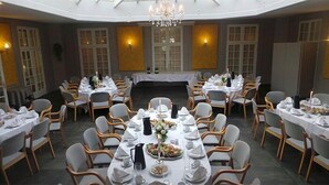 Un comedor formal con mesas redondas, manteles blancos y sillas de madera.