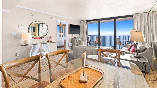 Une chambre d’hôtel moderne avec balcon, une table à manger en verre et un canapé.