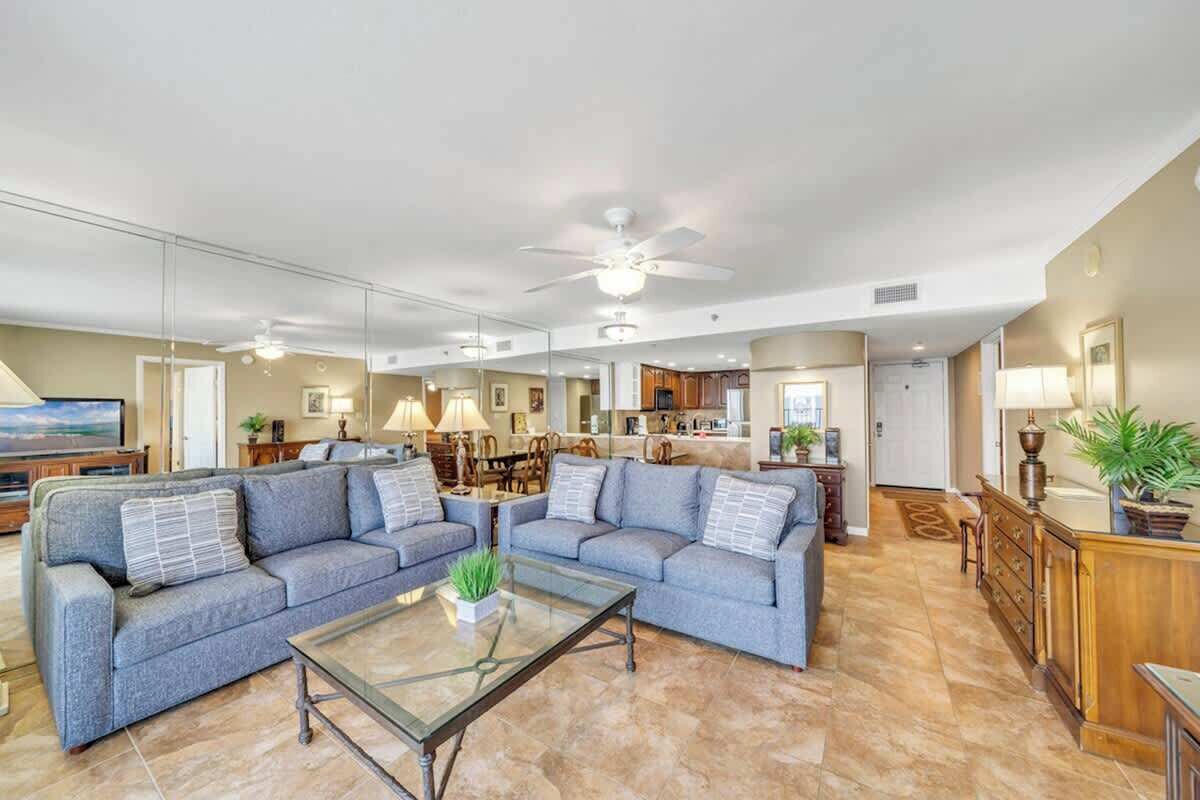 A spacious living room with a large sectional sofa, a glass coffee table, and a ceiling fan.