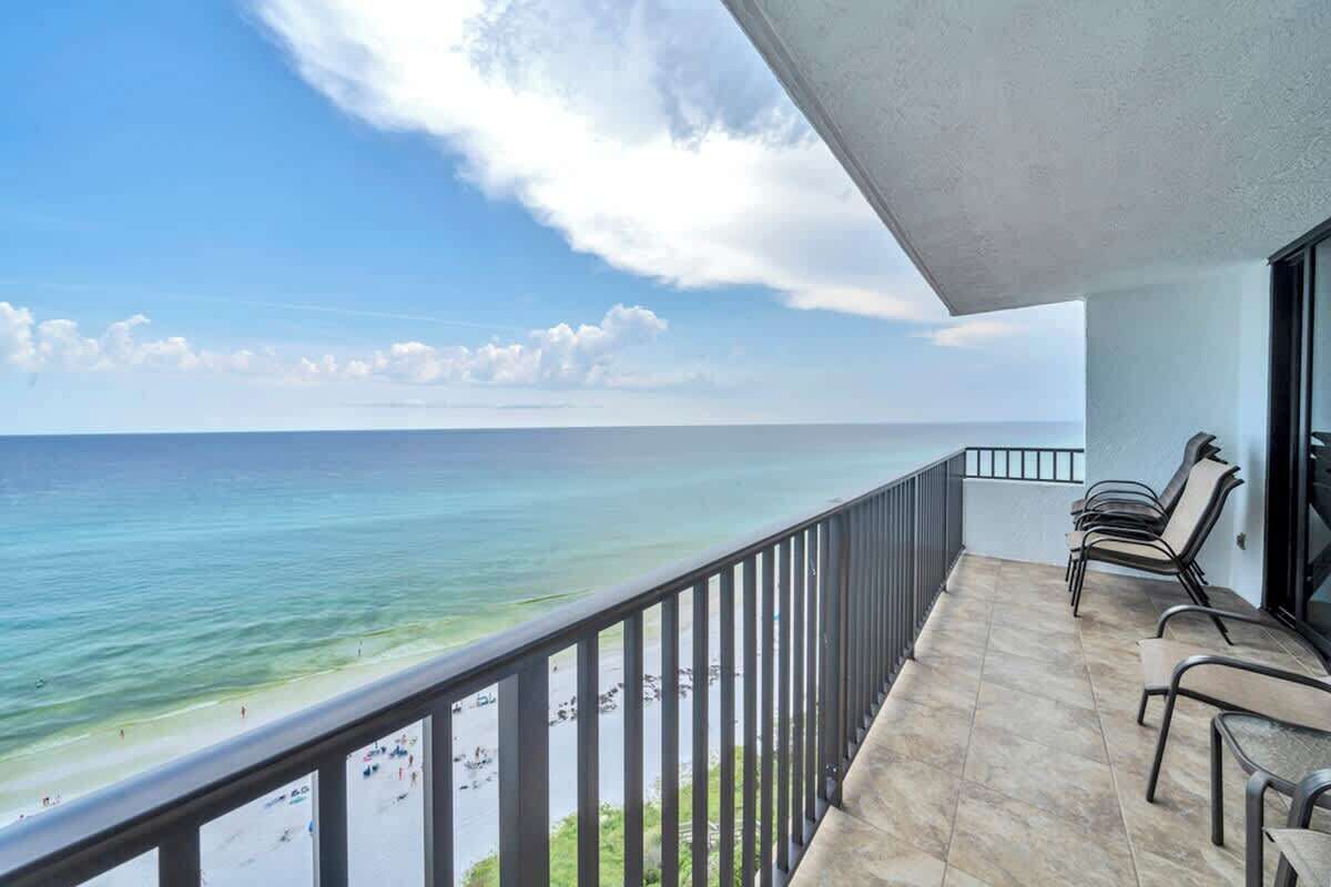 A balcony with a view of the ocean and beach, featuring a tiled floor and metal railings.