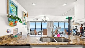 A kitchen with a large window, a sink, and a dining area with chairs.