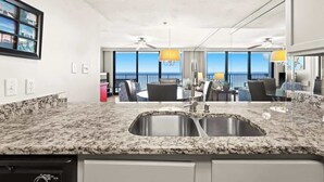 A kitchen with granite countertops, a double sink, and a dining area with a table and chairs. - One Seagrove Place 1507 (Santa Rosa Beach)