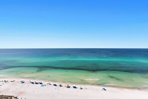 A beach with clear turquoise waters, a sandy shore, and several blue umbrellas. - One Seagrove Place 1507 (Santa Rosa Beach)