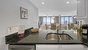 A modern kitchen with a large island, stainless steel sink, and a dining area with a view.