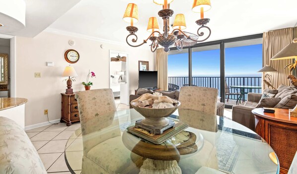Un salon spacieux avec une table basse en verre, des sièges confortables, un lustre et un balcon offrant une vue dégagée.