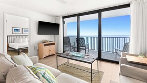 A modern hotel room with a balcony, a flat-screen TV, a bed, a sofa, and a dining area.