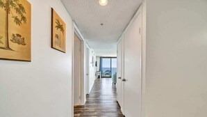 A hallway with wooden flooring, white walls, and framed artwork. - One Seagrove Place 1306 (Santa Rosa Beach)