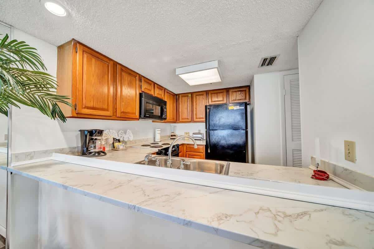 A modern kitchen with wooden cabinets, a stainless steel sink, and a black refrigerator.