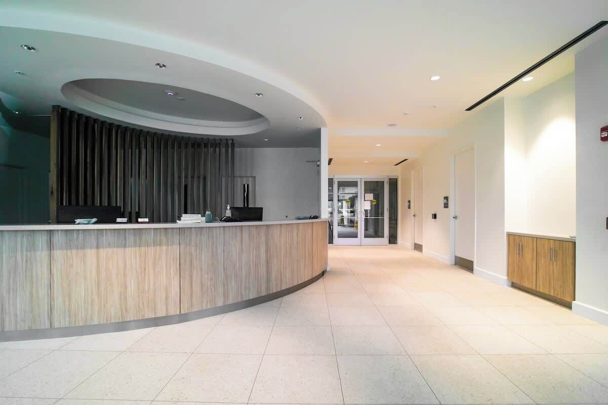 A modern reception area with a curved reception desk, a wooden panel wall, and a glass door leading to a hallway.