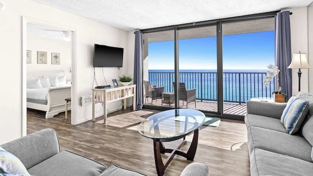 A modern hotel room with a balcony, a flat-screen TV, a sofa, and a glass coffee table. - One Seagrove Place 1306 (Santa Rosa Beach)