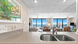 A modern kitchen with granite countertops, a double sink, and a dining area with a view of the ocean. - One Seagrove Place 1103 (Santa Rosa Beach)
