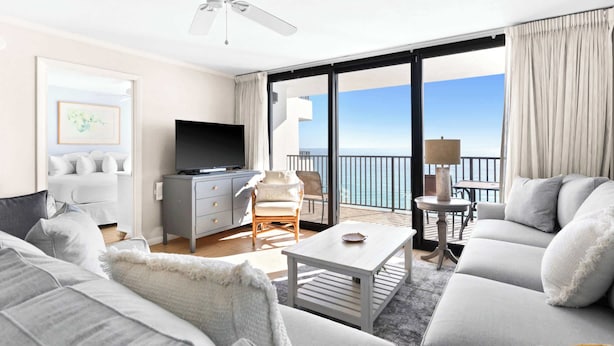 A modern hotel room with a balcony, a flat-screen TV, a sofa, and a dining table. - One Seagrove Place 1103 (Santa Rosa Beach)