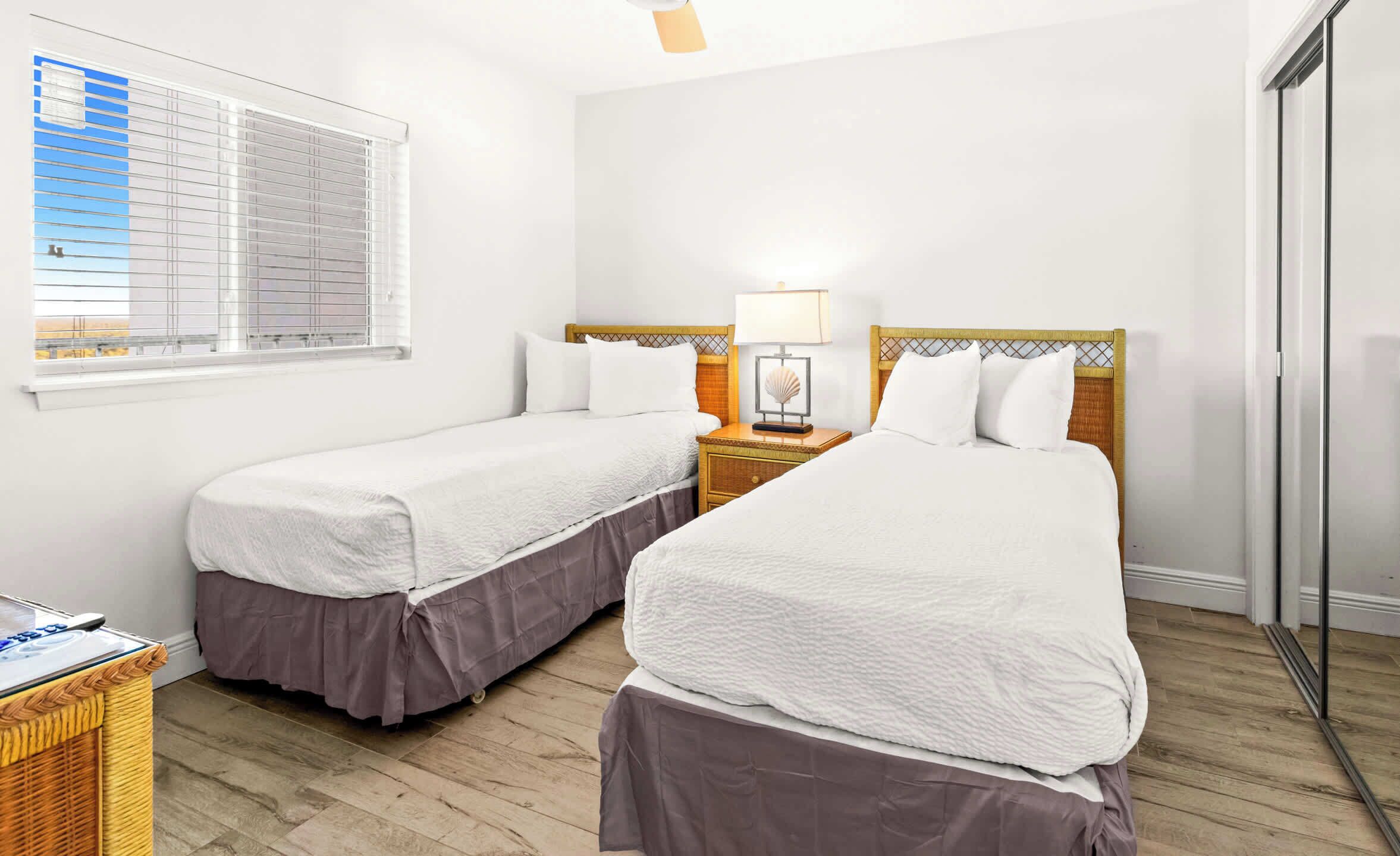 Una habitación de hotel con dos camas individuales, una mesita de noche con lámpara, una ventana con persianas y suelo de madera.