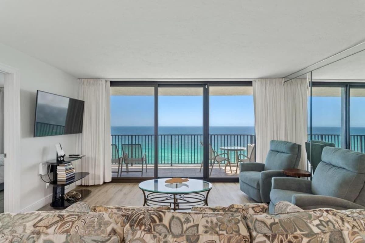 Ein modernes Hotelzimmer mit großem Balkon, Flachbildfernseher, rundem Couchtisch und einer Couch.