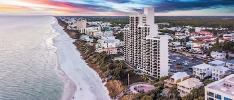 An aerial view of a coastal town with a beachfront, high-rise buildings, and a mix of residential and commercial structures.