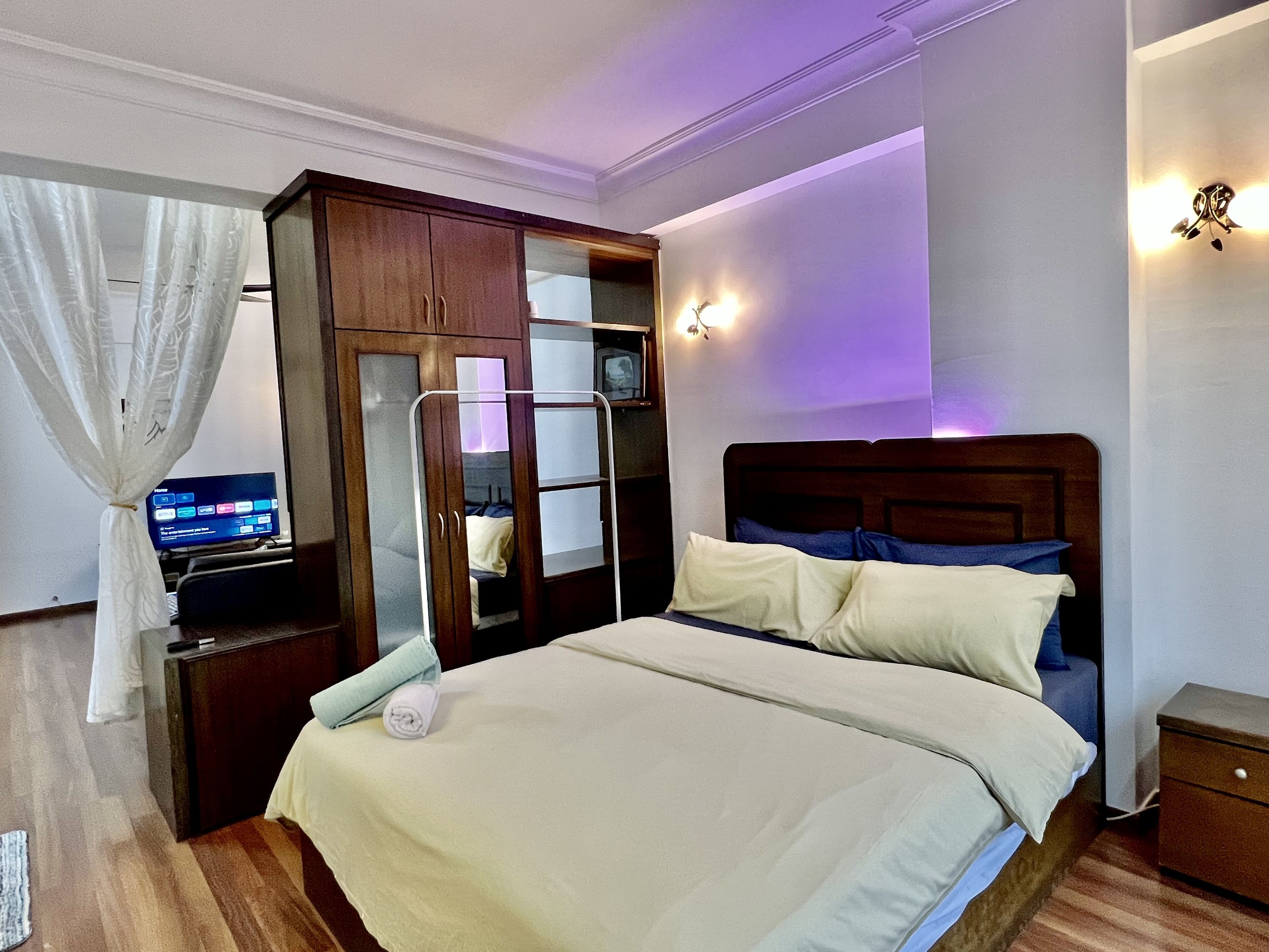 Un dormitorio ordenado con cama, armario, mesita de noche y lámpara de pared.