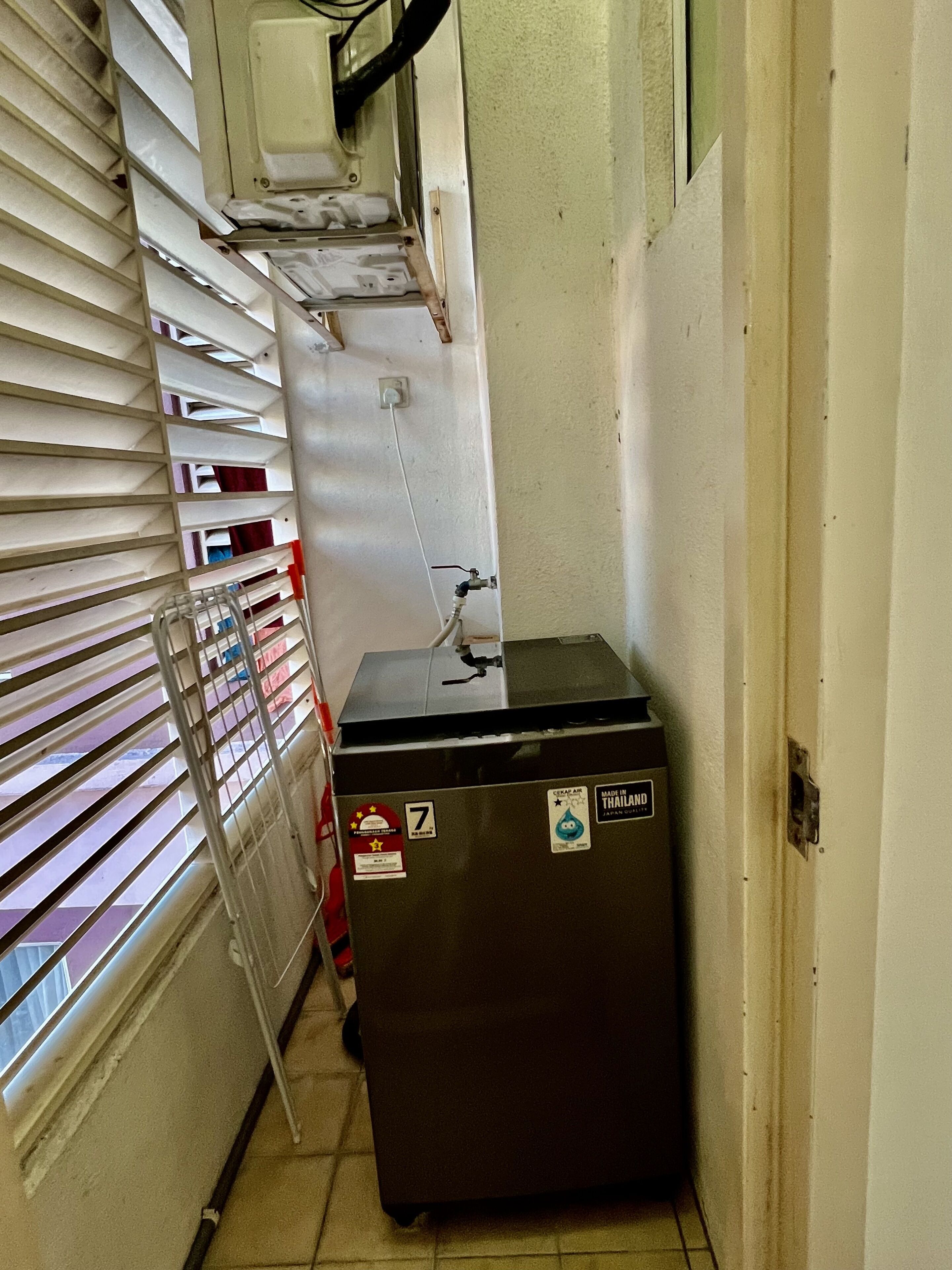 A narrow hallway with a metal rack of folded towels, a small refrigerator with a water dispenser, and a window with blinds.