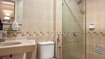 Un baño con ducha de vidrio, lavamanos con espejo e inodoro.