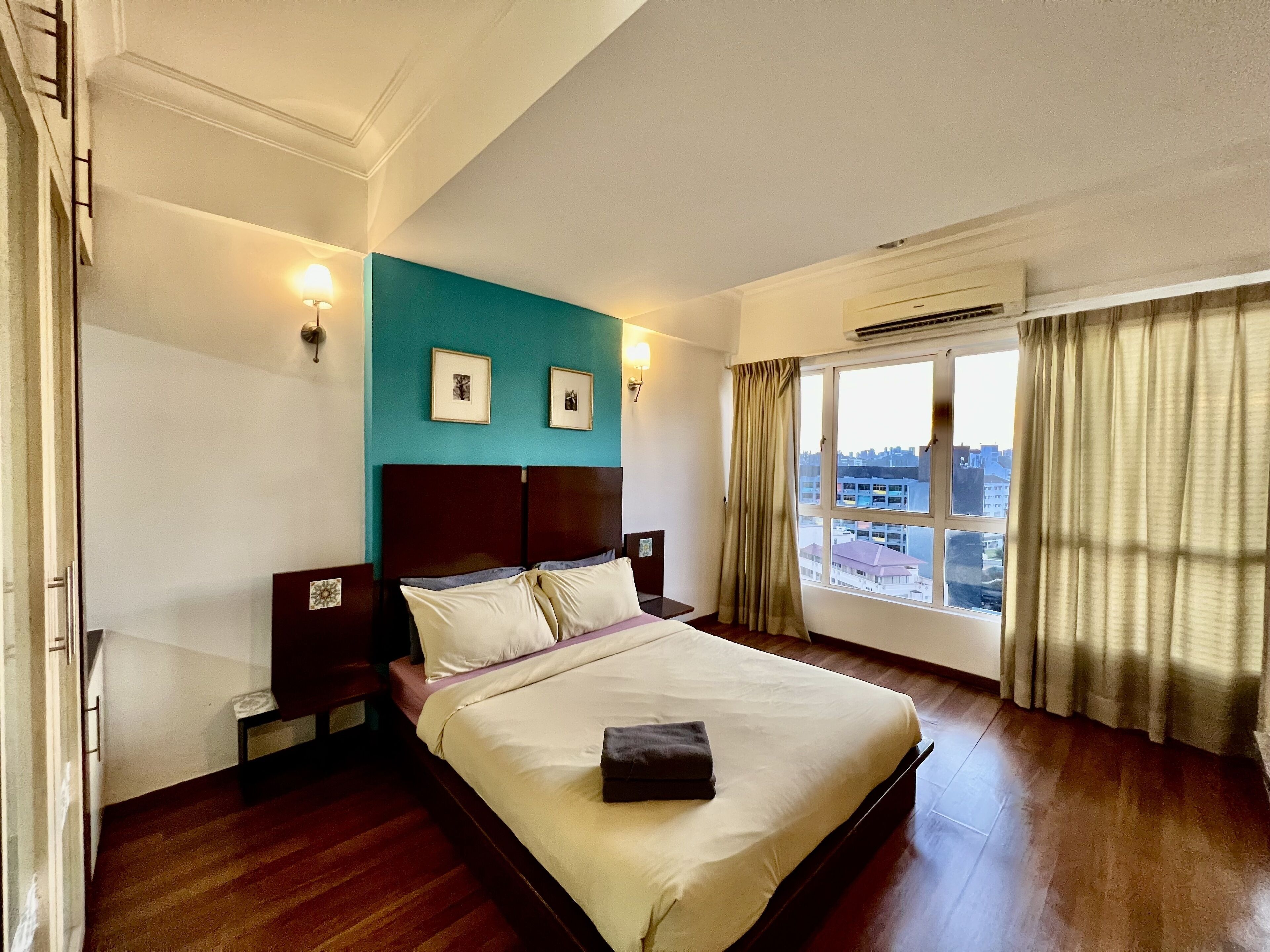 Habitación de hotel con una cama grande, una pared de acento color aguamarina, dos mesitas de noche con lámparas y una ventana con cortinas.