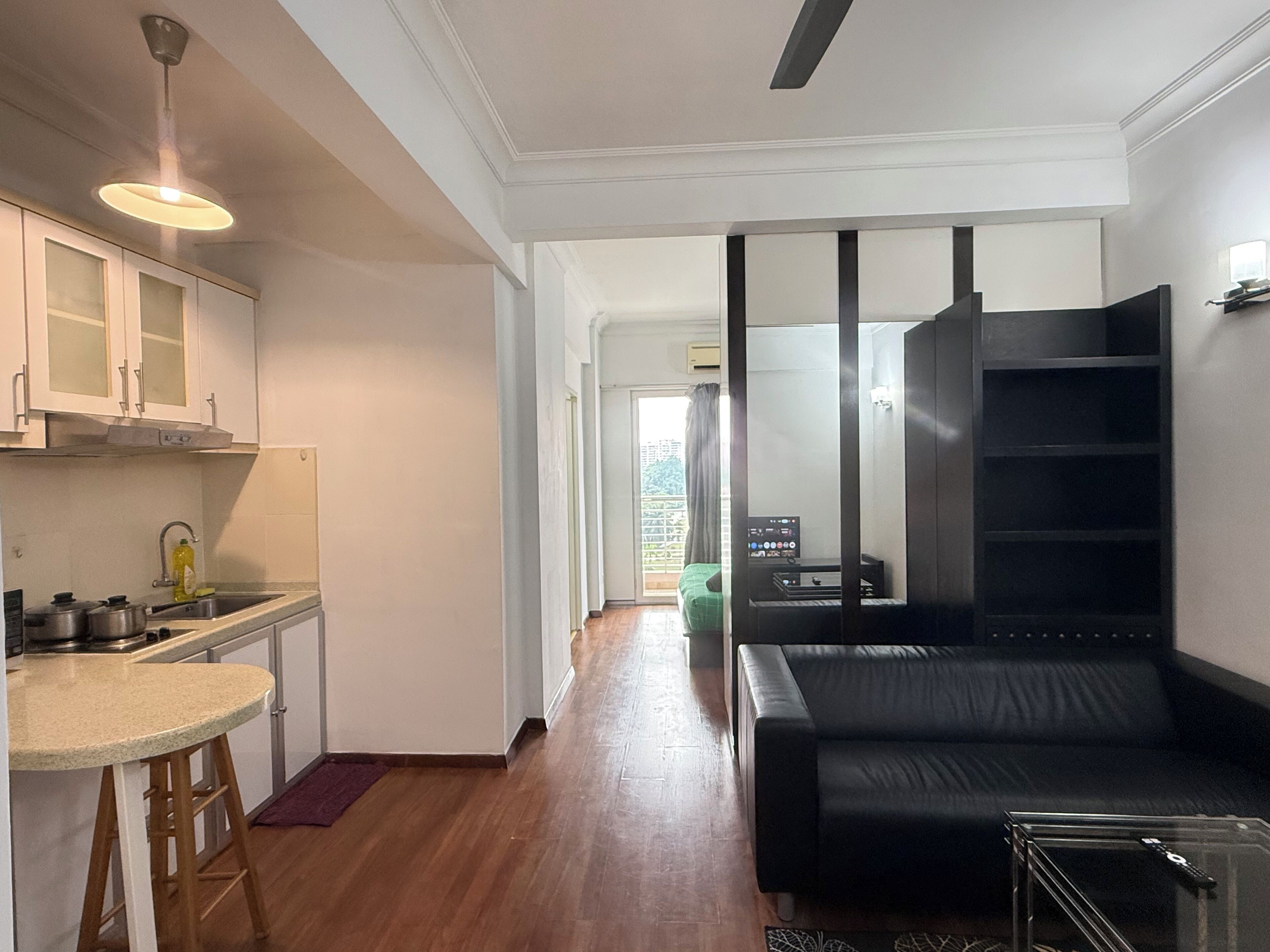 Un apartamento moderno con cocina, zona de estar con un sofá negro y un mueble de entretenimiento pequeño.