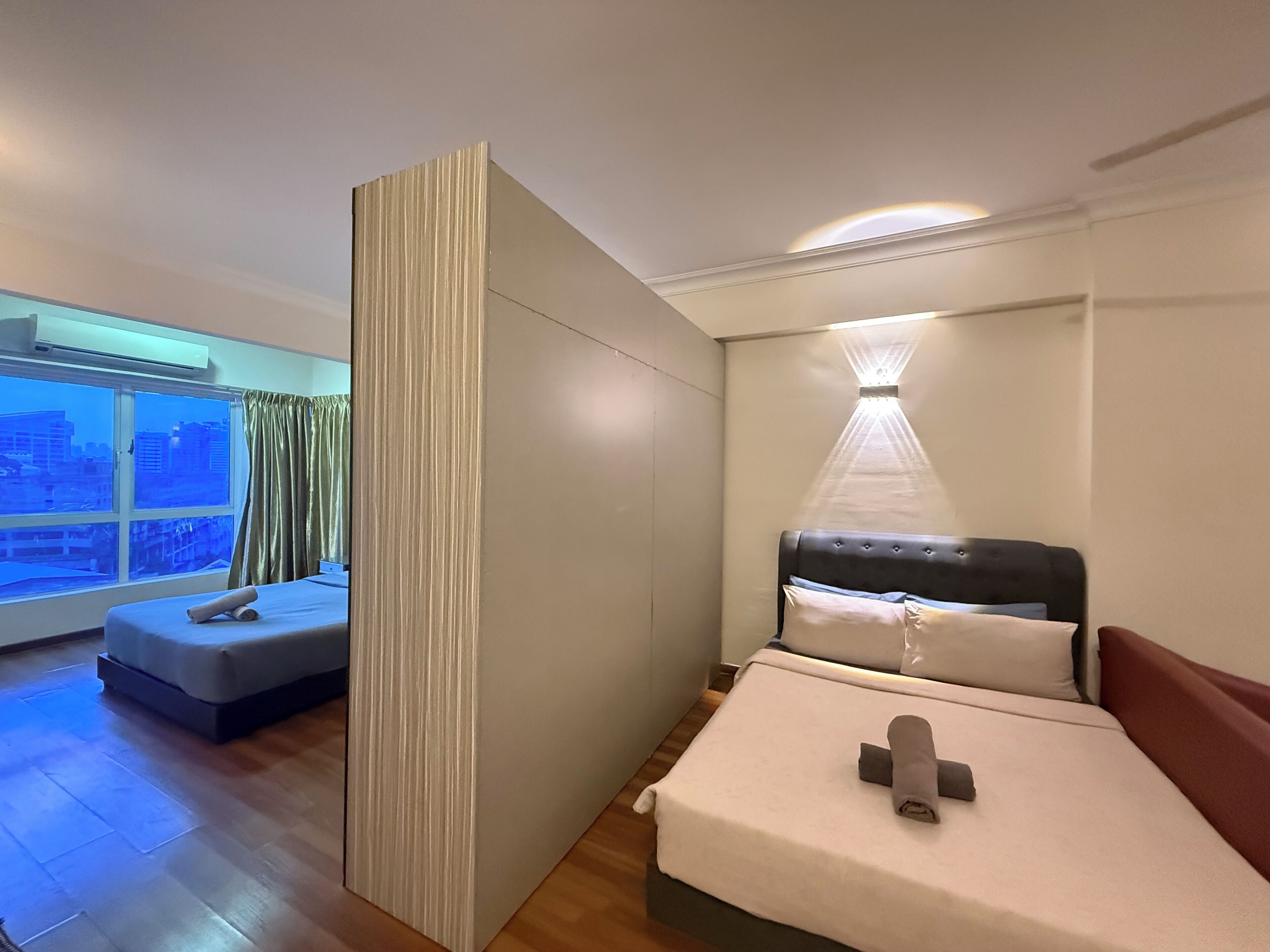 Una habitación de hotel con una cama, una ventana con cortinas, una mesita de noche y un aplique de pared.
