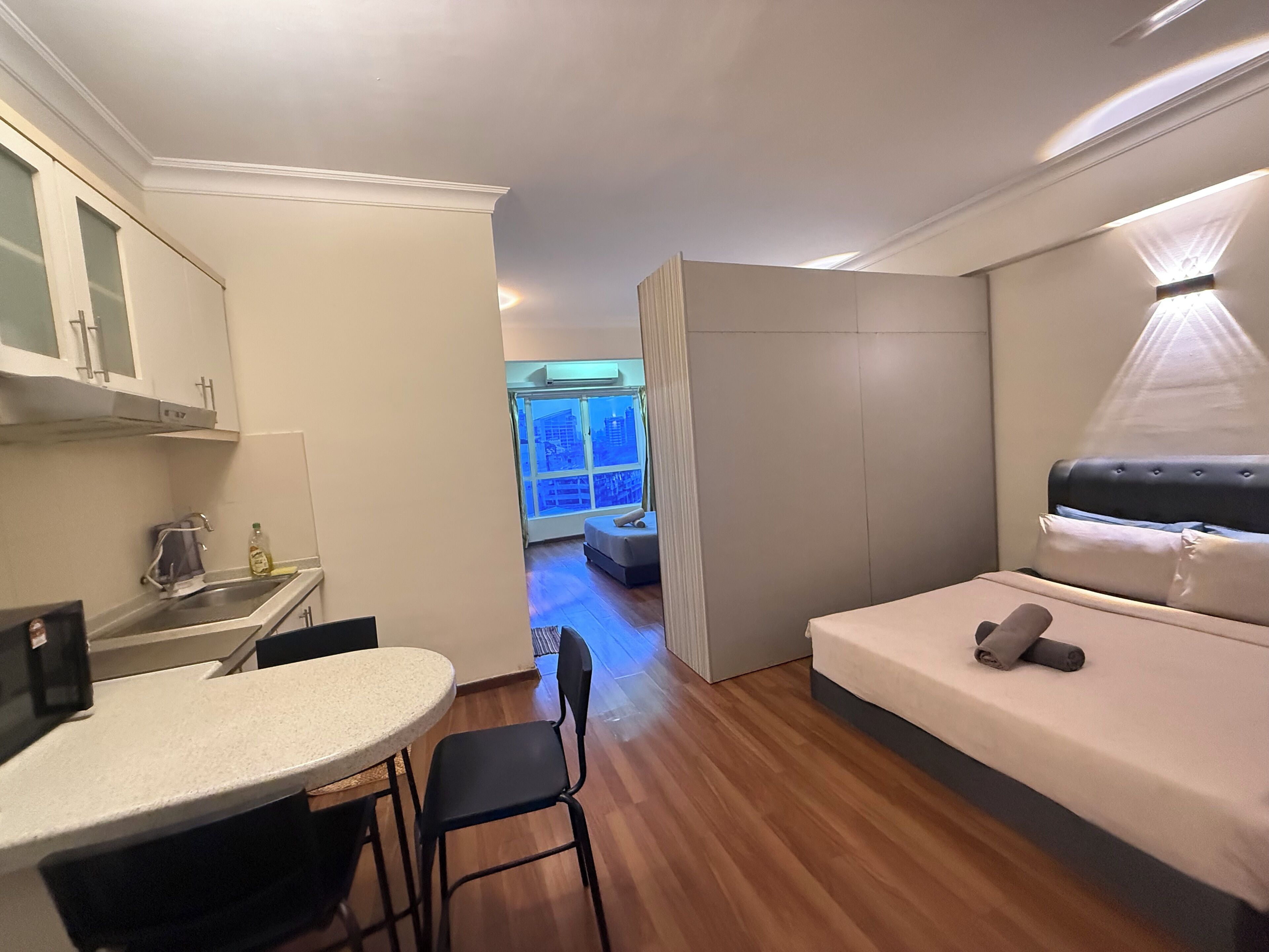 Una habitación compacta con kitchenette, una cama y vistas de la ciudad a través de un ventanal grande.