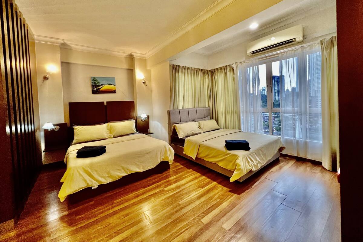 Habitació d'hotel amb dos llits, terra de fusta, aire condicionat, vista a la ciutat per la finestra i un quadre a la paret.