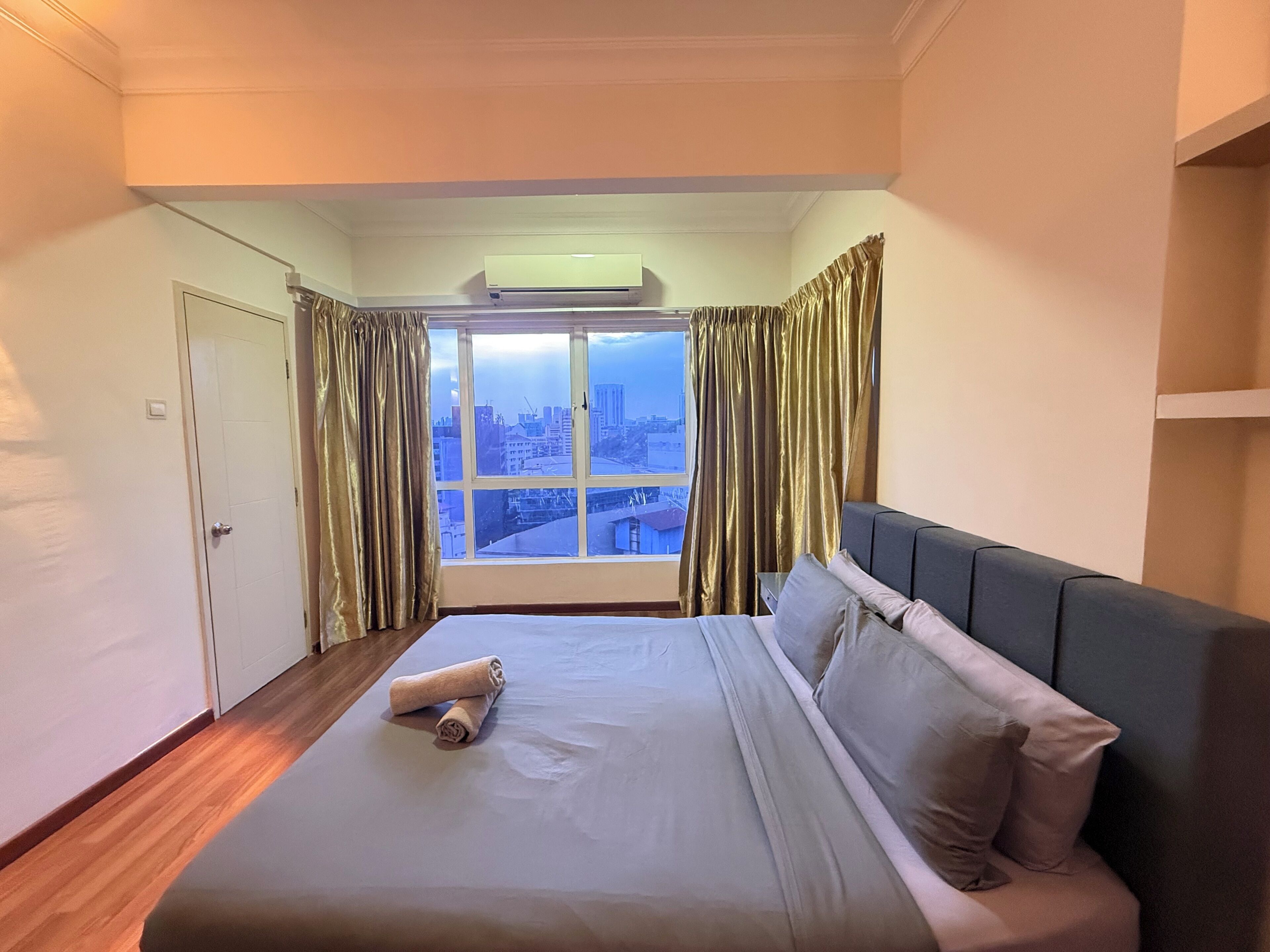 A hotel room with a large bed, a window with curtains, and a view of the cityscape.