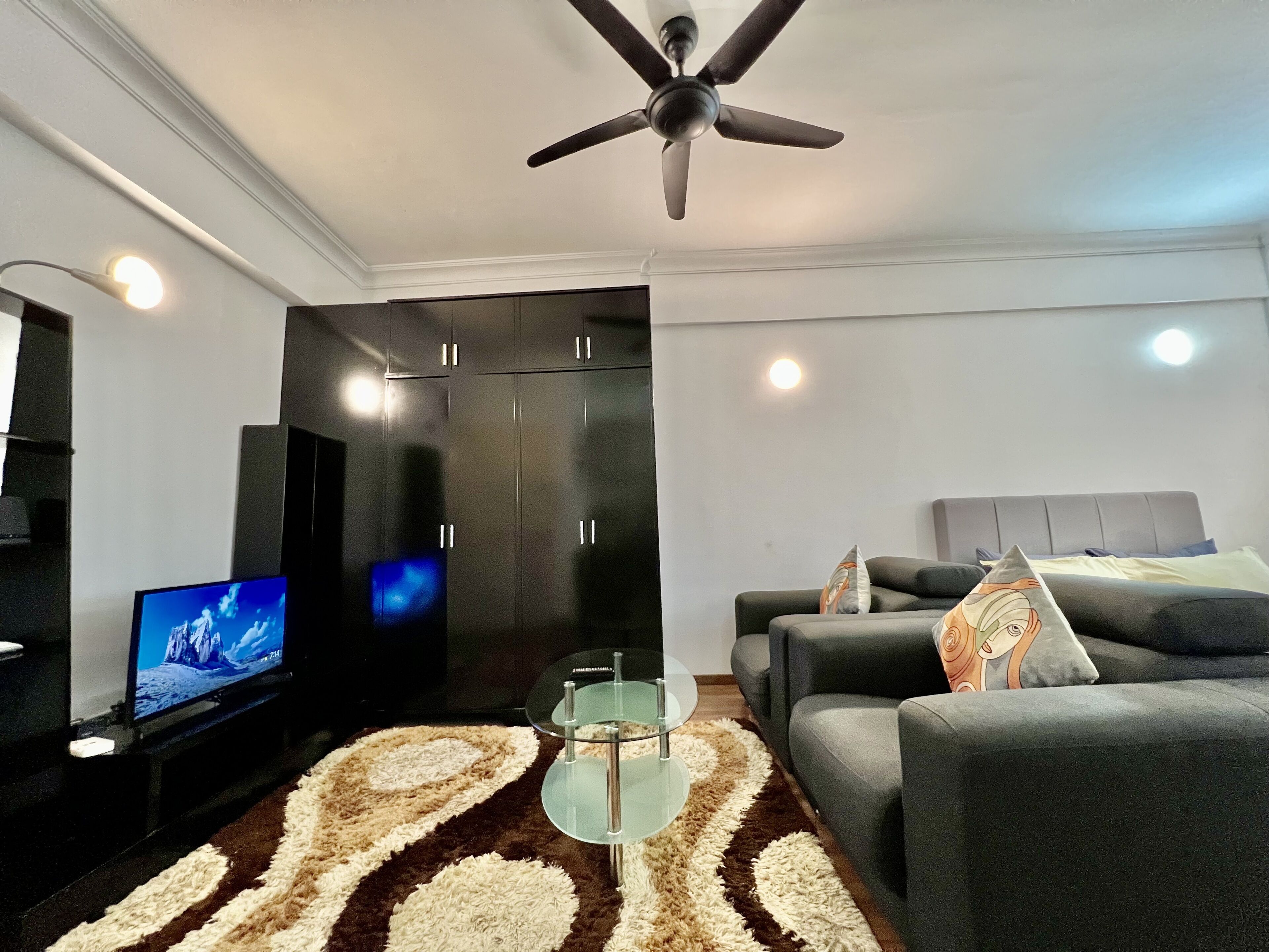 A modern living room with a flat-screen TV, a ceiling fan, a sofa, and a patterned rug.