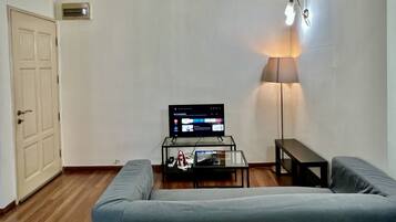 Una sala de estar con un sofá, una mesa de centro con un televisor, una lámpara y una puerta.