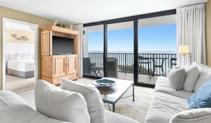 Quarto de hotel com varanda, televisão, sofá e mesa de jantar.