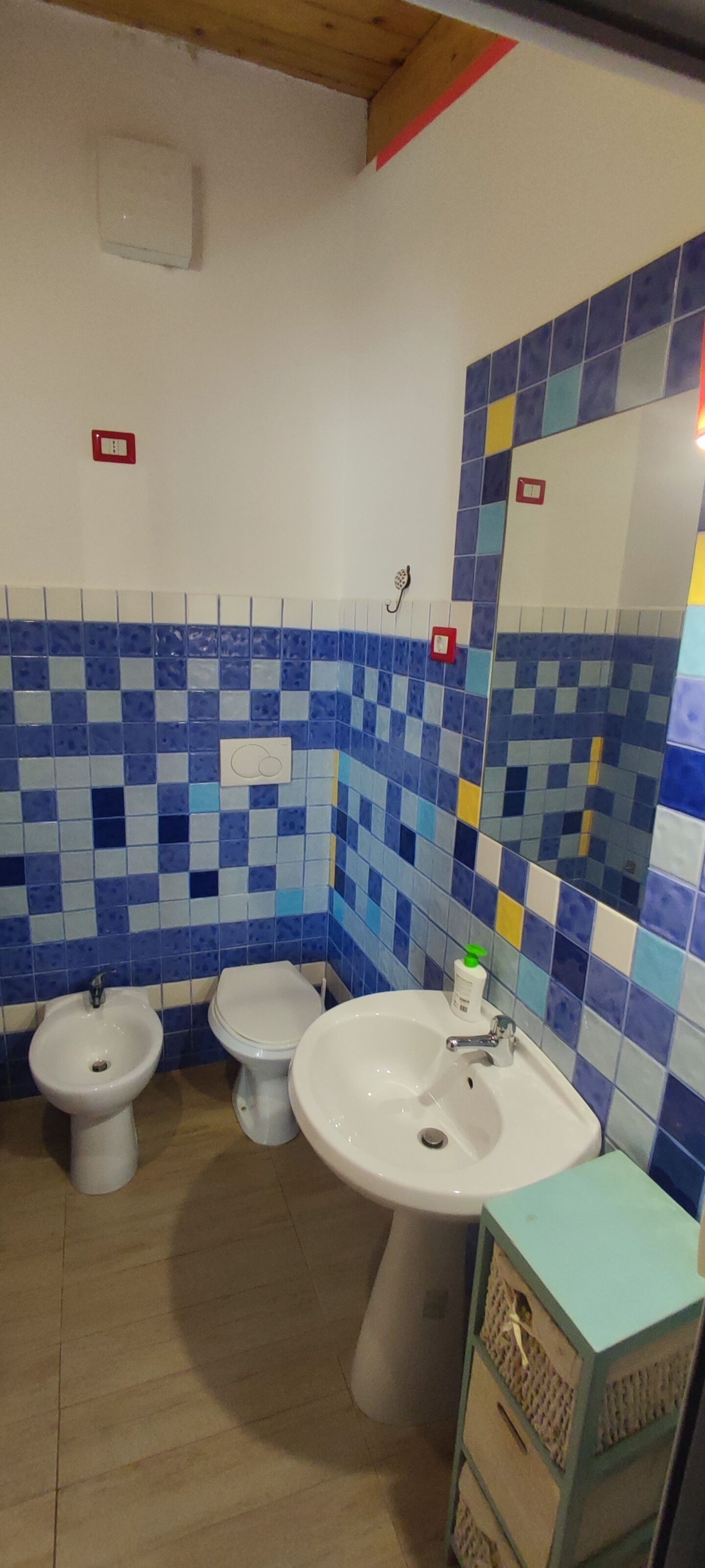 Een badkamer met een blauw-wit betegelde muur, een wit wastafelmeubel, twee toiletten en een spiegel.