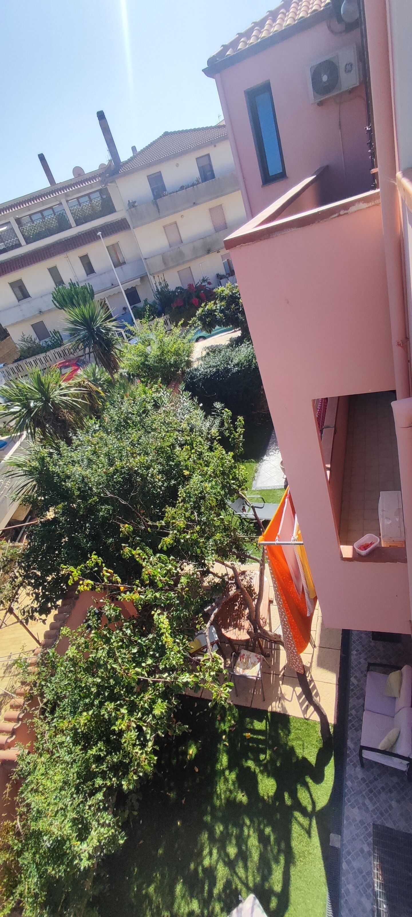 Een woongebouw met balkon, een klein terras met tuinmeubilair en een tuin met diverse planten.
