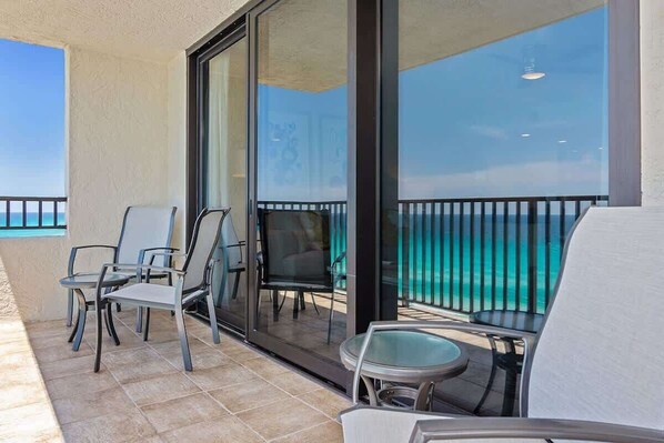 A balcony with a glass door, two chairs, a small table, and a view of the ocean. - One Seagrove Place 0806 (Santa Rosa Beach)
