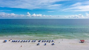 A beach with rows of blue umbrellas and a few red umbrellas, indicating a beach resort setting.