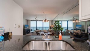 A modern kitchen with a large island, stainless steel sink, and overhead pendant lighting. - Family Beachfront Corner Unit Sleeps 6 (Santa Rosa Beach)