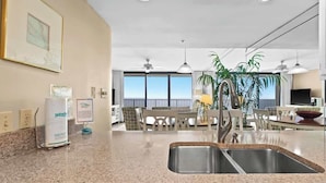 A modern kitchen with granite countertops, a double sink, and a dining area with a view of the sky.
