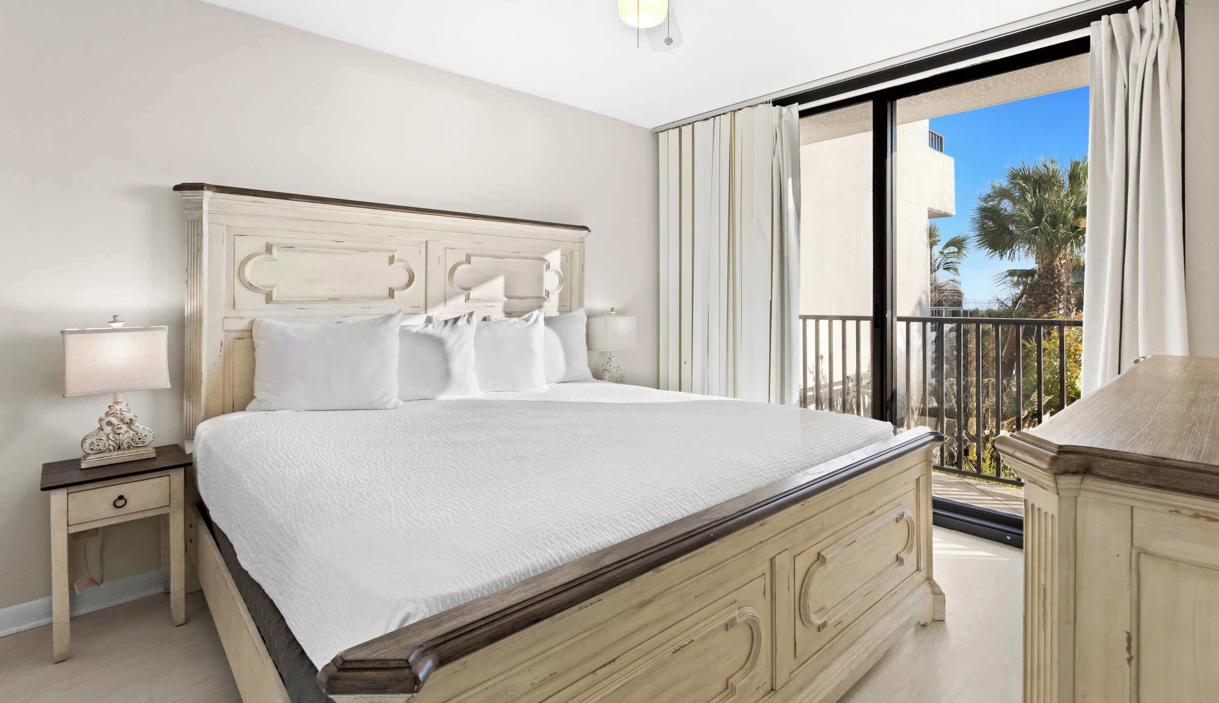 Une chambre avec un grand lit, une table de chevet avec une lampe et une vue sur l’extérieur grâce à un balcon.