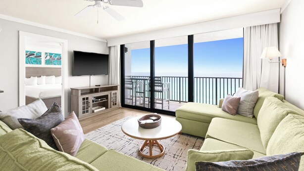 A modern hotel room with a balcony, a flat-screen TV, a sofa, and a coffee table.