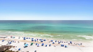 A beach with numerous umbrellas and sun loungers, a wooden boardwalk, and a clear view of the ocean.