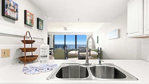 A modern kitchen with a double sink, wicker baskets, a bottle of green heritage, and a balcony with a view.